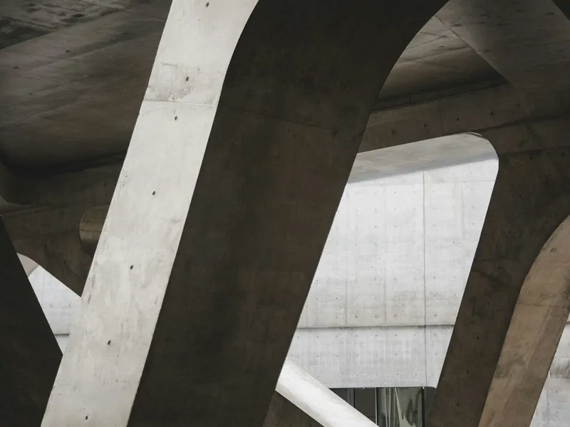 Structure porteuse en béton brut, piliers et poutres entrecroisés en lumière naturelle