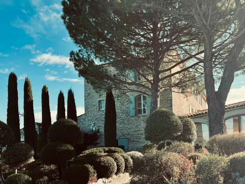 Mas provençal en pierre restauré, façade en pierre de taille entourée de cyprès, de topiaires et d'un grand pin