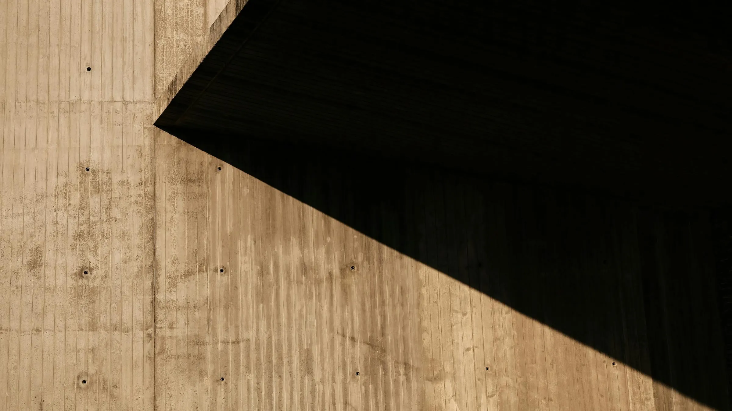 Détail de mur en béton banché brut texturé, lumière rasante révélant la matière