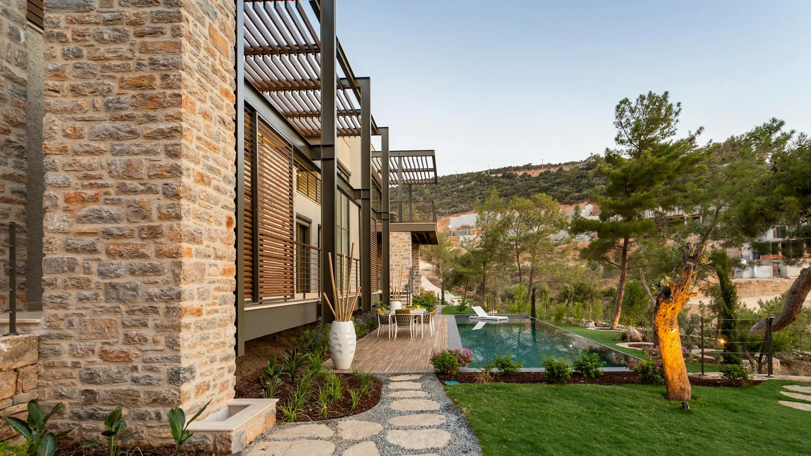 Villa contemporaine en pierre avec pergola en bois et piscine, jardin paysager méditerranéen en lumière douce